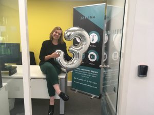 D7LrCJkXoAExbmz Janina Neumann sitting on her desk, smiling at the camera, holding a balloon shaped as a 3